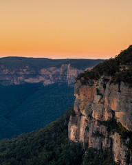 Fototapeta na wymiar Golden sunrise across orange sandstone cliffs above eucalyptus trees in the Gross Valley in the Blue Mountains, west of Sydney, Australia