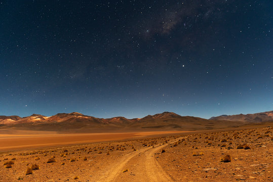 The Milky Way at night on the road in the Siloli Desert with the Andes mountain peaks in the background, Uyuni Salt Flat region, Bolivia. 