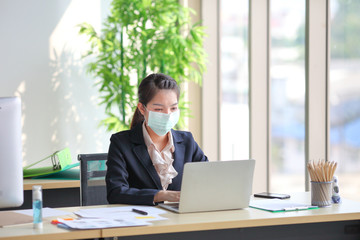 Female employee wearing medical face mask while working alone because of social distancing policy in the business office during coronavirus or covid-19 outbreak pandemic situation