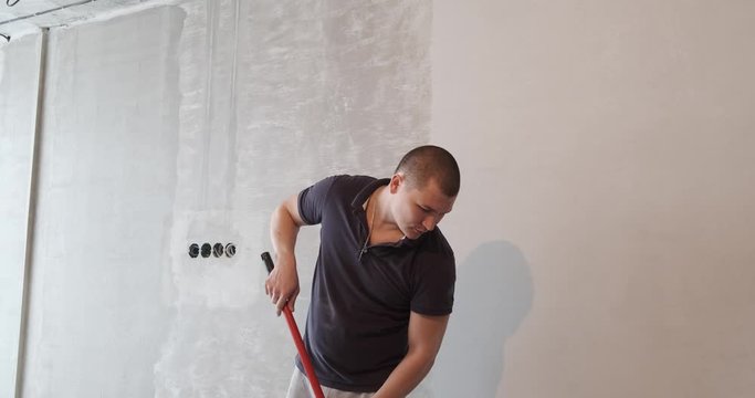 Repairman is preparing wall for painting. Using tool, he puts putty on wall. Young man works builder, he does it well. If you need high-quality repairs. Profession of builder is available to everyone