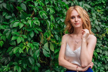 Portrait of a young beautiful woman, standing next to the wall of wild grape leaves.