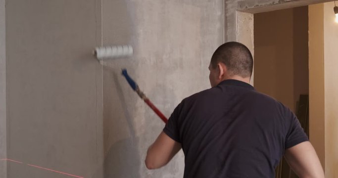 Builder prepares wall in repair apartment. Using tool, he puts putty on gray wall. Quality at every stage of repair is future of comfortable apartment. Builder does his job professionally. Repairman