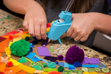 Child using hot glue gun to place purple felt on a rainbow collage