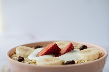 Healthy breakfast, bowl of oatmeal and yogurt with strawberry, banana and dried raisins