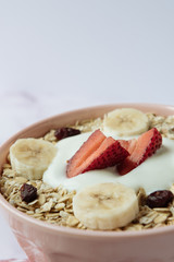 Healthy breakfast, bowl of oatmeal and yogurt with strawberry, banana and dried raisins