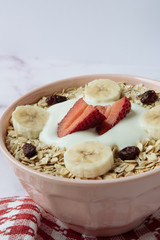 Healthy breakfast, bowl of oatmeal and yogurt with strawberry, banana and dried raisins
