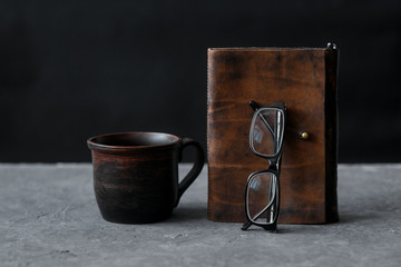 Brown leather notebook and glasses on wooden table. Businessman workspace with cup of black coffee....