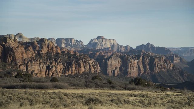 A golden hour timelapse of shadows rolling over red cliffs in Zion National Park which are illuminated in golden sunlight.