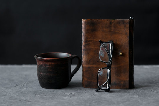 Brown leather notebook and glasses on wooden table. Businessman workspace with cup of black coffee. Business planning and work day organization. Coffee break at workplace in office