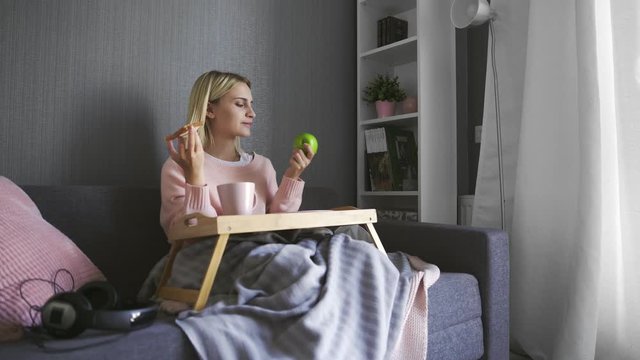 Young woman sits on couch and makes a choice what to eat toast with chocolate or apple
