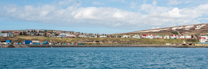 Panorama shot from the sea towards the charming city of Husavik in northern Iceland. Houses and snow covered mountains during spring time.