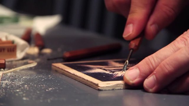 Artist carves a woodblock print with carving tools in the background.