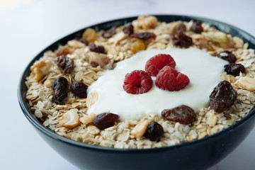 Healthy breakfast, bowl of oatmeal and yogurt with raspberry, nuts and dried raisins