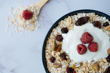 Healthy breakfast, bowl of oatmeal and yogurt with raspberry, nuts and dried raisins