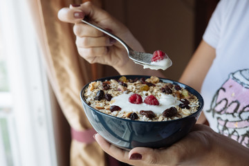Healthy breakfast, a woman holds in her hands a bowl of oatmeal and yogurt with raspberry, nuts and dried raisins