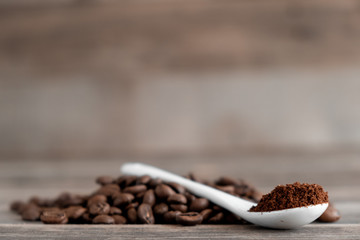  white ceramic spoon with ground coffee on a wooden background Fried Arabica grains
