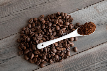  white ceramic spoon with ground coffee on a wooden background Fried Arabica grains