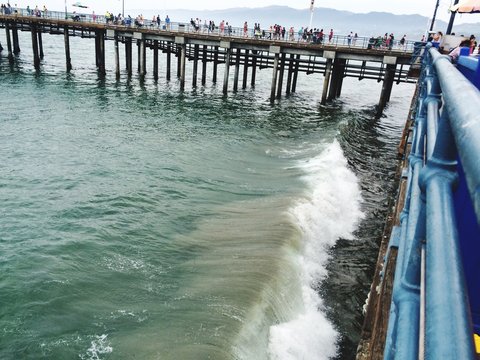 Side View Of People Walking On Bridge At Calm Sea