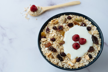 Healthy breakfast, bowl of oatmeal and yogurt with raspberry, nuts and dried raisins