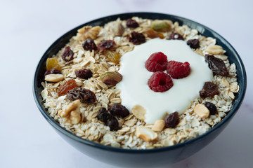 Healthy breakfast, bowl of oatmeal and yogurt with raspberry, nuts and dried raisins