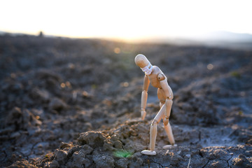 Tired wooden mannequin with face mask on dry soil, corona virus, death and life concept.