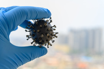 hand with glove catching a coronavirus model in front of buildings