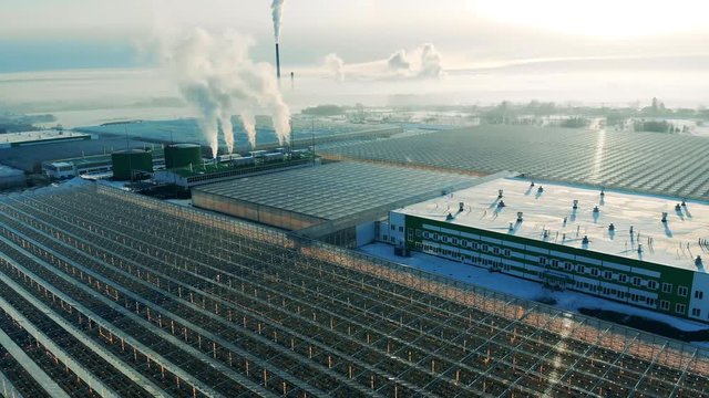 Outdoors view of glasshouse facilities with billowing chimneys. Power factory from above, steam from a smokestack.