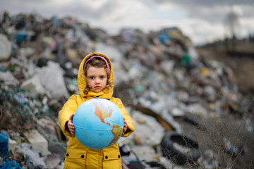 Small child holding globe on landfill, environmental pollution concept.