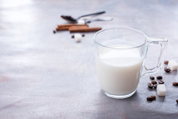 Delicious and fragrant coffee with a glass cup of milk, sticks of fragrant cinnamon, coffee beans, sugar cubes ob the table