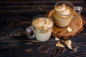 Delicious and fragrant dalgona coffee in glass cups, cinnamon sticks, dried mushrooms, a spoon of instant coffee, sugar. Cooling coffee drink with milk