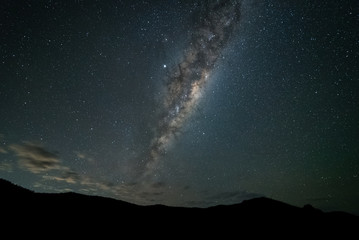 A night time photo of the Milky Way galaxy rising above mountains against a dark starry sky in the...