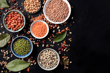 Legumes flatlay assortment, shot from above on a black background with copy space. Lentils, soybeans, chickpeas, red kidney beans, a vatiety of pulses
