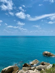 ocean, big rocks against the background of blue sky and white clouds on a tropical island in summer