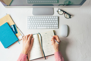Hands notes the date in the calendar. Office desktop top view. Professional occupation. Work from home. Work and vacation planning