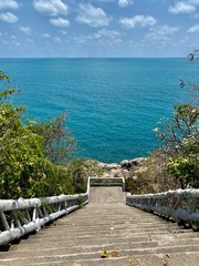 Fototapeta premium white staircase on the observation deck leading to the sea against a blue sky with white clouds and green trees under the sun in the tropics