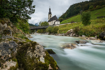 Fototapeta na wymiar A landscape view of a beautiful flowing river in Ramsau Germany, with a little church in the background
