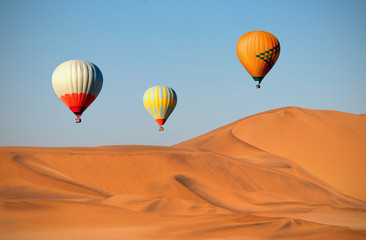 Colored hot air balloons flying over the sand dunes at sunset