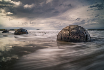Waves washing against the mysterious Moeraki Boulders with dark storm clouds overhead at Koekohe beach on the Otago coast of New Zealand. These amazing round stones were formed millions of years ago © Matthew