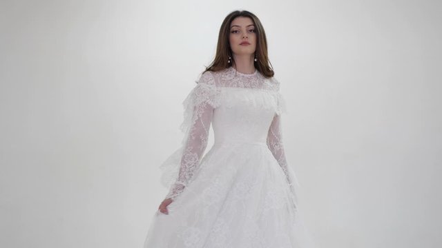 professional model in long wedding dress with lacy sleeves and bodice poses for camera in studio slow motion