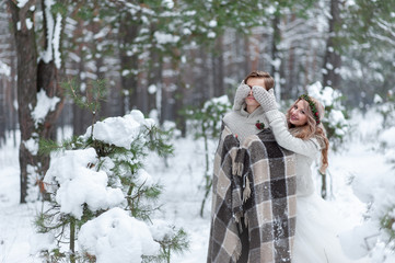 Cute girl covering boyfriend's eyes by her knitted mittes. Winter wedding.