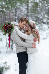 Bride and groom in beige knitted pullovers in snowy forest. Newlyweds is touching foreheads. Winter wedding. Copy space