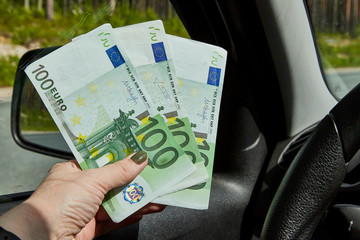 Euro banknotes of various denominations in a woman hand inside of a car