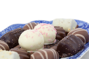 Selection of chocolates on a blue and white patterned plate.  On a white wood background