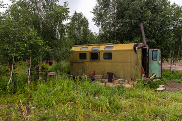 Fototapeta na wymiar An old car booth converted into a house in the forest. Green iron shed with windows and chimney. The door is open. Around the green trees and grass. Horizontal.