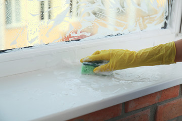 Fototapeta na wymiar Woman cleaning window sill with sponge, closeup