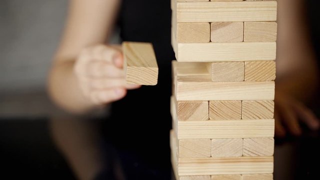 Games at home: A beautiful girl plays with her cute daughter in the jenga tower. They are sitting on the couch in the living room. The girls are laughing and smiling. Child makes her move. Slow motion