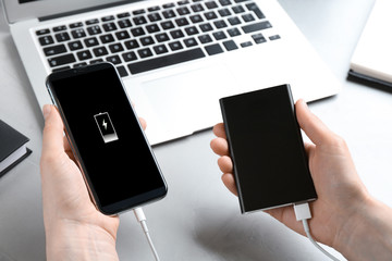 Woman charging mobile phone with power bank at light grey stone table, closeup