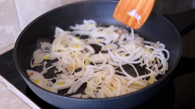 onion fried in the pan with a wooden kitchen spatula