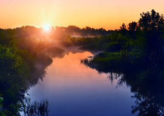 Naklejka na ściany i meble River in the early morning at dawn. Delicate dawn sky and fog rising above the water, lush greenery on the banks. Summer spring wild landscape by the river. Selective soft focus.