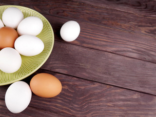Several white and brown eggs in a ceramic plate and next to a plate on an brown wooden table.